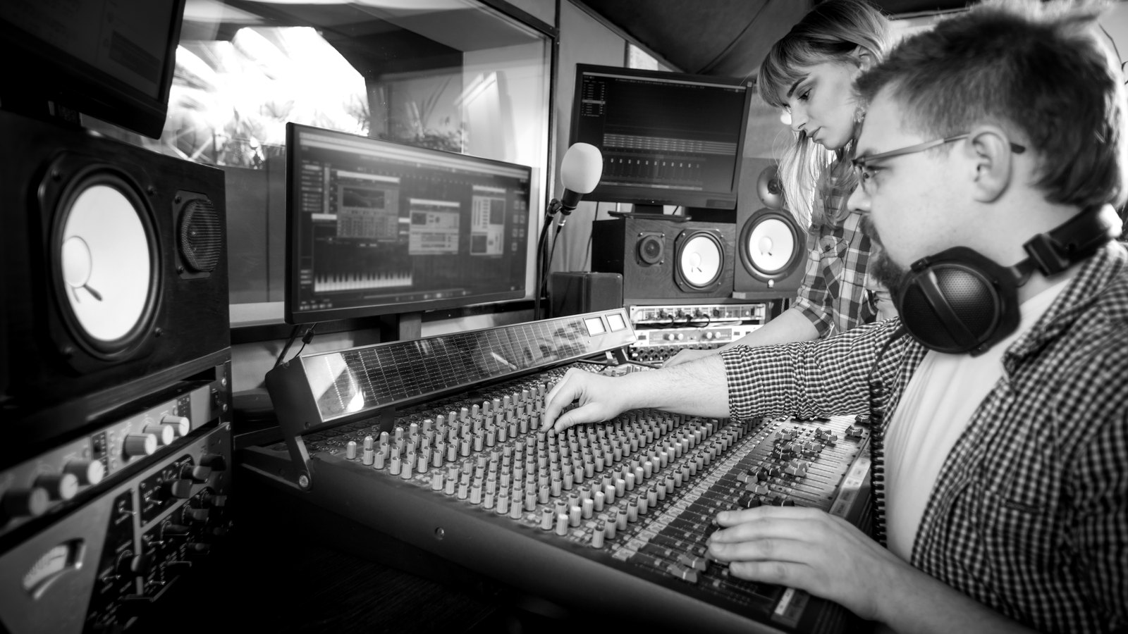A sound engineer and a musician at a large mixing console, working on a track together in a studio control room.